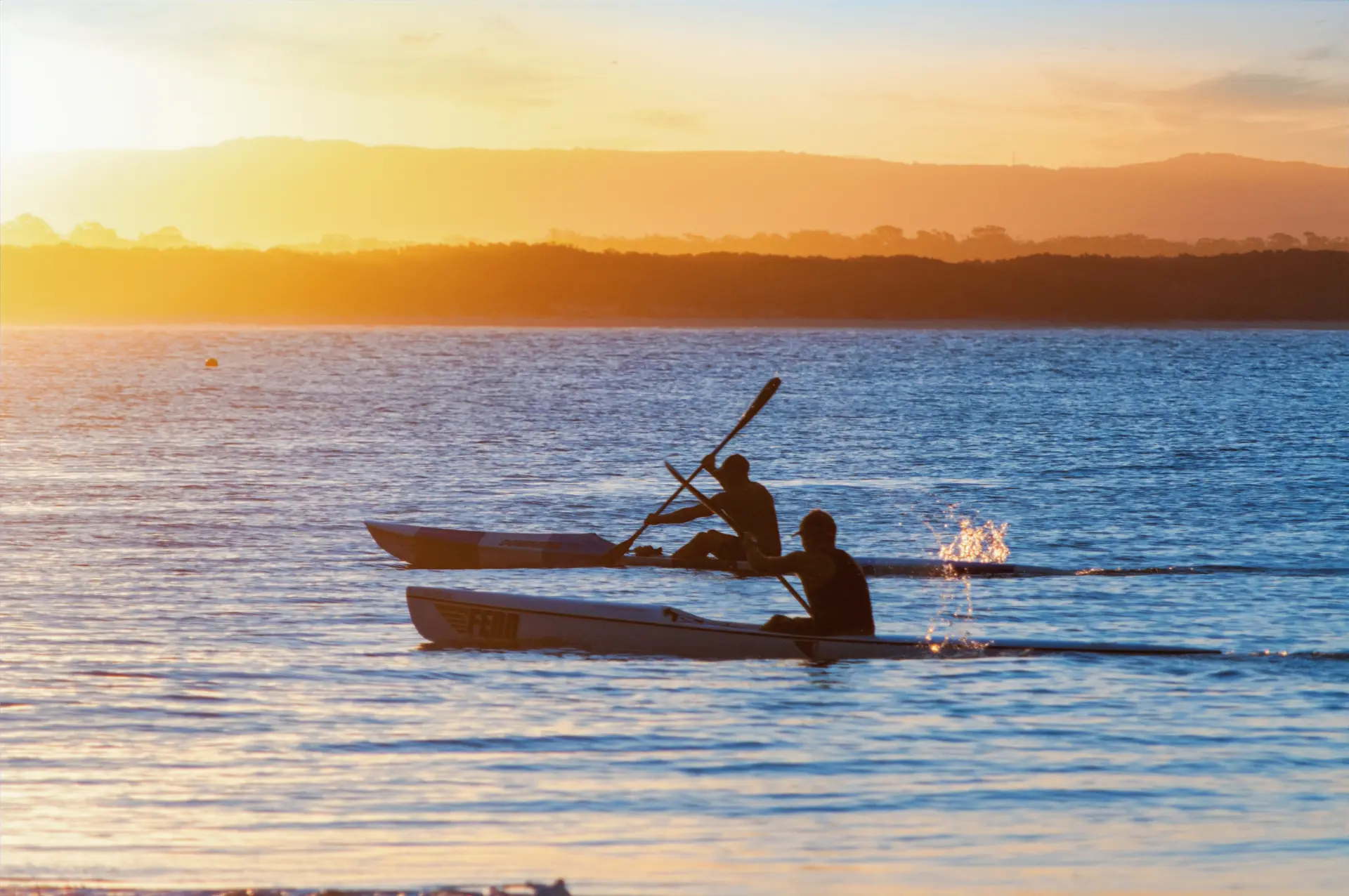 Two kayakers paddling through Noosa beach at sunset