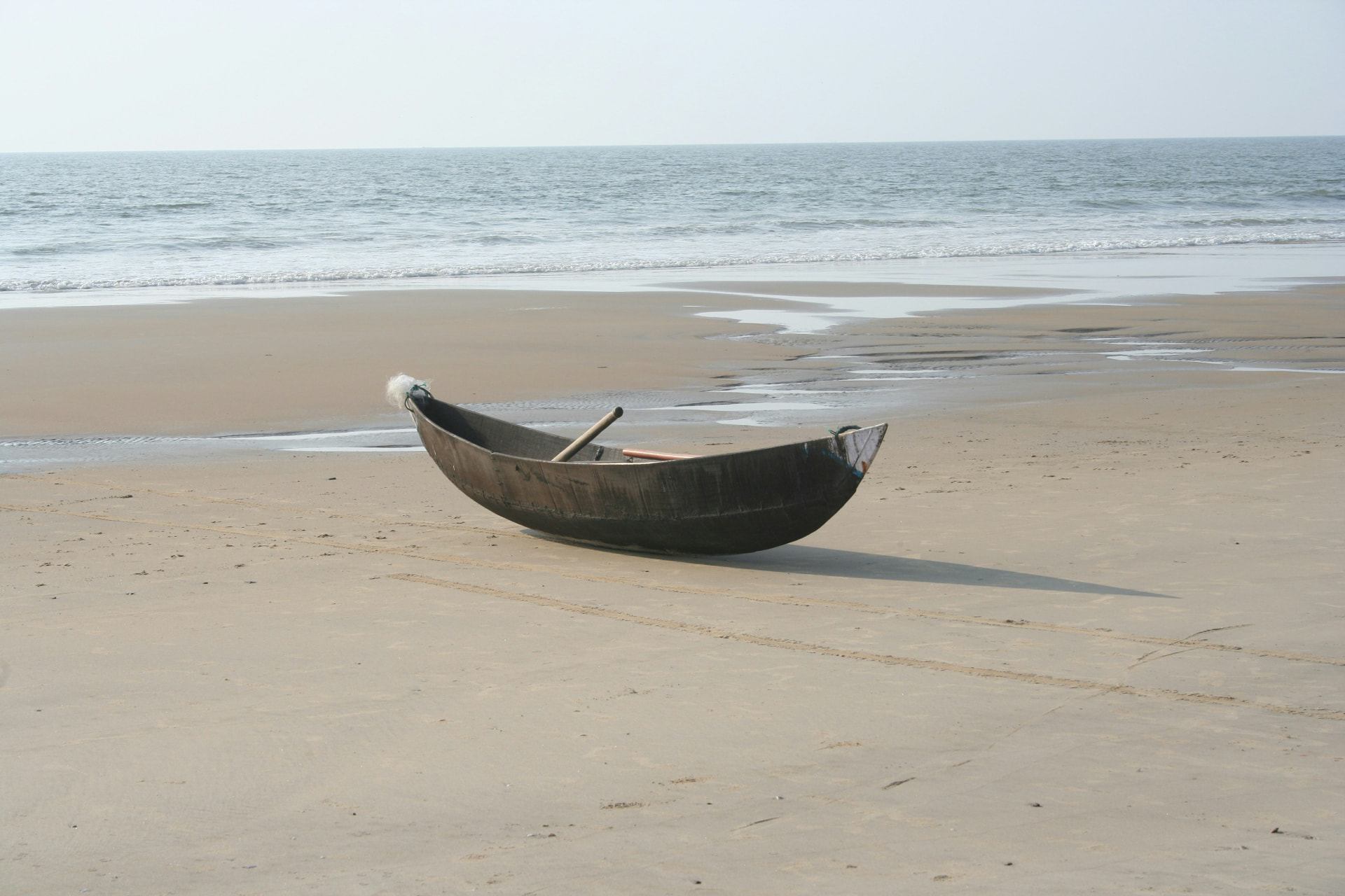 A lone wooden boat resting on a wide, quiet beach at low tide